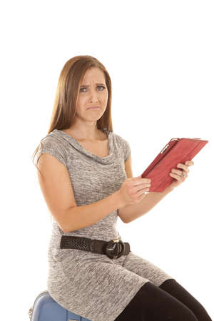 A woman sitting on her luggage with a sad expression on her face holding on to her tablet.の写真素材
