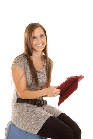 A woman sitting on her suitcase waiting holding on to her tablet with a smile,の写真素材