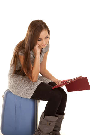 A woman sitting on her suitcase reading something from her tablet.の写真素材