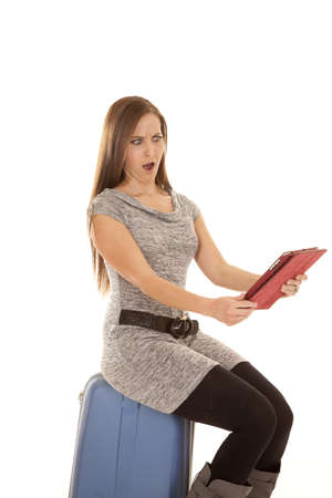 a woman sitting on her luggage with a shocked expression on her faceの写真素材