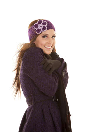 a woman in her winter coat and hat with a smile on her face trying to get warm, with the wind blowing her hair.の写真素材