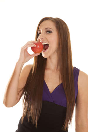 a woman in her purple and black top getting ready to take a big bite out of her appleの写真素材