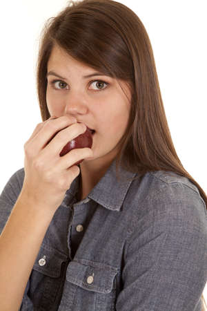 A close up of a woman taking a bite out of an apple with her big eyes.の写真素材