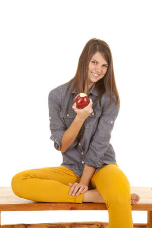 A woman sitting on a bench with a big smile on her face holding on to her appleの写真素材