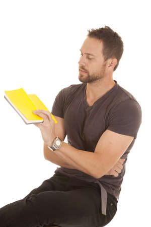 a man sitting on a stool looking at the back of a yellow book.の写真素材