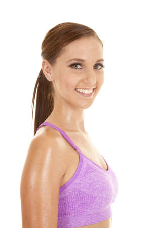 A woman in her purple sports bra with sweat on her arms and a smile on her lips.の写真素材