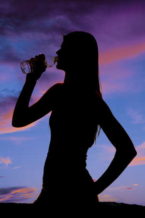 A silhouette of a woman getting a drink from a water bottle.の写真素材