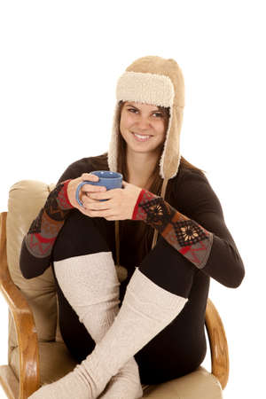A woman sitting in her chair in her warm clothes and hat holding on to a mug with a warm drink.の写真素材