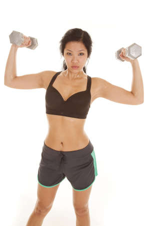 An Asian woman with a serious expression on her face lifting weights and sweat dripping off of her body.の写真素材
