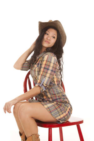 An Asian woman sitting on her red chair in her plaid dress and wearing her cowgirl hat.の写真素材