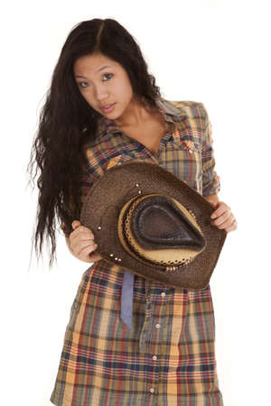 An Asian woman holding on to her hat in her plaid dress and serious expression.の写真素材