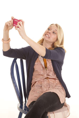 a woman sitting in a blue chair holding up her phone and taking a picture of her cheesy smile.の写真素材