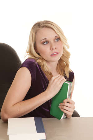 A woman sitting at her desk holding on to a green book with a faraway look in her eyesの写真素材