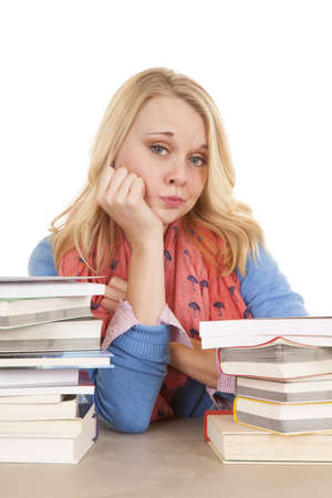 A woman sitting at a desk with stacks of books with a bored expression on her face.の写真素材