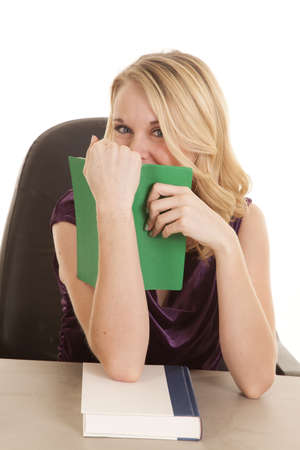 A woman with her eyes smiling looking over the top of the book.の写真素材