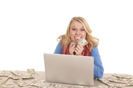 a woman with her laptop and money everywhere smiling big.の写真素材