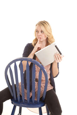 A woman sitting on a chair holding on to her tablet with her finger up to her lips.の写真素材