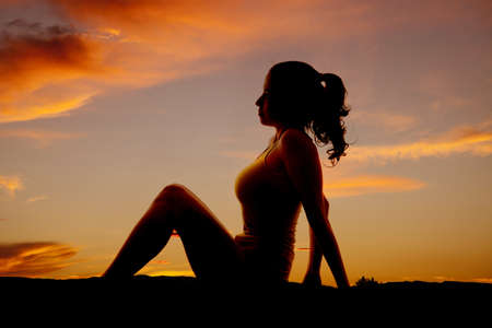 A woman is sitting in the sunset with her knees up.の写真素材