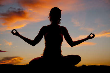 A woman is sitting in a yoga pose silhouetted in the sunset.の写真素材