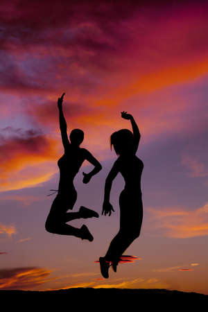 A silhouette of two women jumping and having fun infront of a beautiful sunset.の写真素材