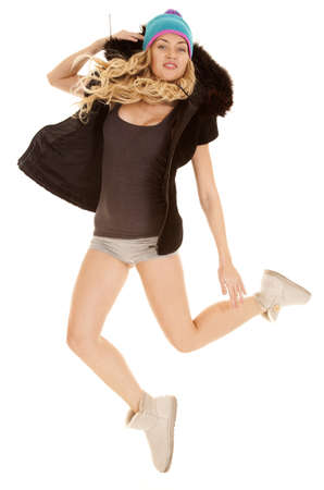 A woman in her boots, coat and winter hat jumping in the air with a smile on her face.の写真素材