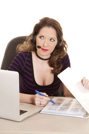 A woman with a headset is sitting by a laptop with a pen and binder.の写真素材