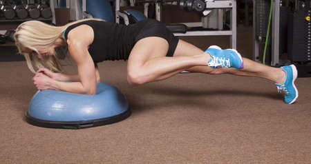 a woman in plank on a half of a ball bringing her knee to her arm.の写真素材