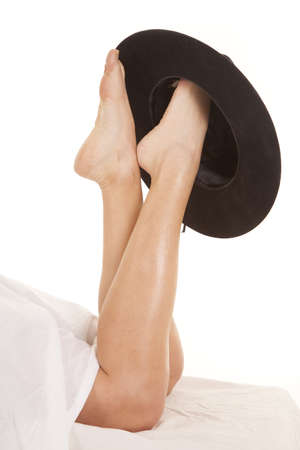 A woman with her legs coming out from under a sheet with a cowboy hat on her foot.の写真素材