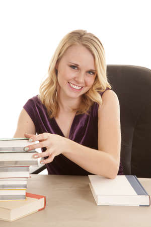 A woman with a big smile on her face sitting at her desk with a big stack of books.の写真素材