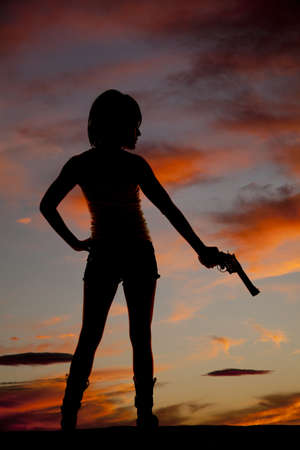 A silhouette of a woman standing and holding onto a pistol.の写真素材