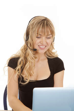 A woman with a smile on her face with her headset and working on her computerの写真素材