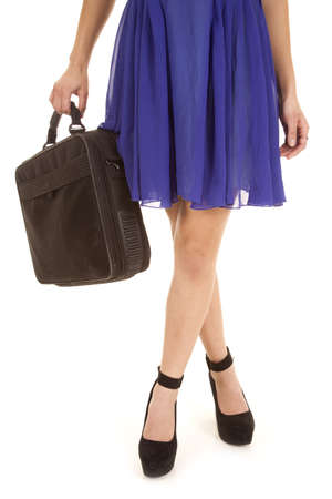 a woman standing with her legs crossed holding on to her bag.の写真素材
