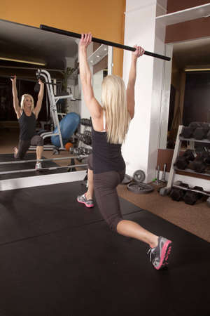 A woman working out in the gym lifting a bar while she is lunging.の写真素材