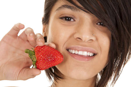 a close up of a woman with a smile on her face holding on to a strawberry up by her mouth.の写真素材