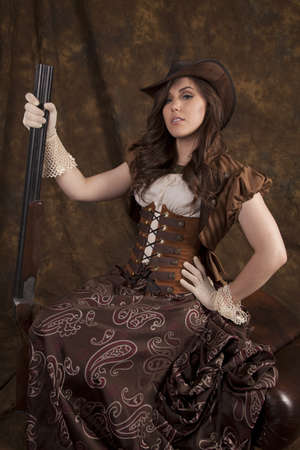 A woman in her beautiful western dress and corset holding on to her shot gun being a real cowgirl.の写真素材