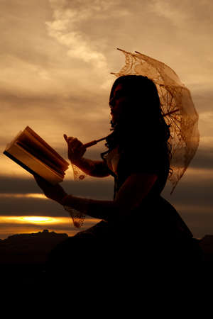 A silhouette of a woman using the last light of day to read a book out in the sunset.の写真素材
