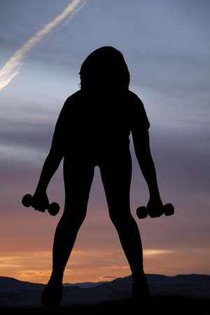 A silhouette of a woman working out with weights with a beautiful sunset in the background.の写真素材