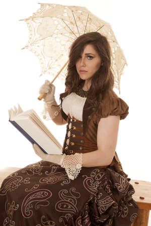A woman sitting on a bench reading a book and holding onto her umbrella with a sad expression on her face.の写真素材