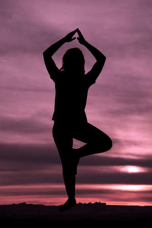 A woman doing yoga outdoors with a beautiful sunset in the background.の写真素材