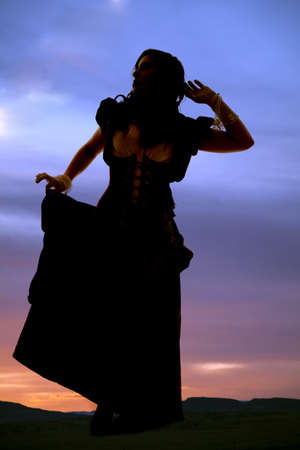 A woman standing and holding on to her skirt looking into the sky.の写真素材
