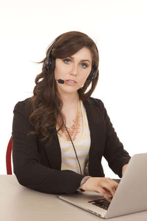 a woman looking at the camera and typing on the laptop with her head set on.の写真素材