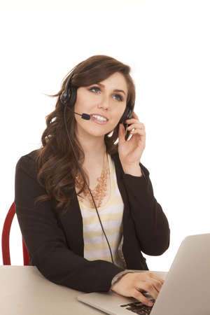 A woman working on her laptop and talking on her headset with a smile on her face.の写真素材