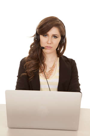 A woman sitting at her desk talking on her headset working on her laptop.の写真素材