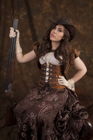 a woman in her vintage western dress holding on to a shotgun with a serious expression on her face.の写真素材