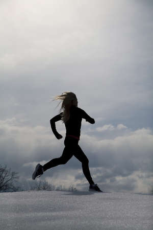 A silhouette of a woman running through the snowの写真素材