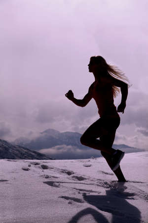 A silhouette of a woman running through the snow with mountains in the background.の写真素材