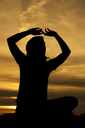 A silhouette of a woman holding her arms up doing yoga in the outdoors.の写真素材