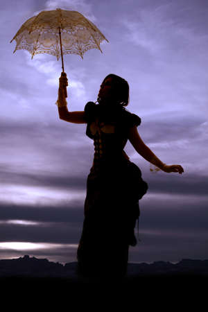 A silhouette of a woman in her vintage dress holding on to her umbrella in a beautiful skyの写真素材