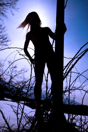 A silhouette of a woman standing up by a pole with the sun behind her.の写真素材