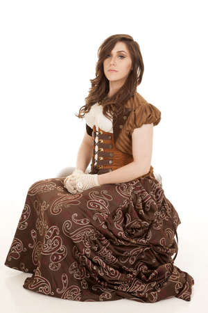 a woman sitting on a stool in her vintage clothing with a serious expression on her face.の写真素材